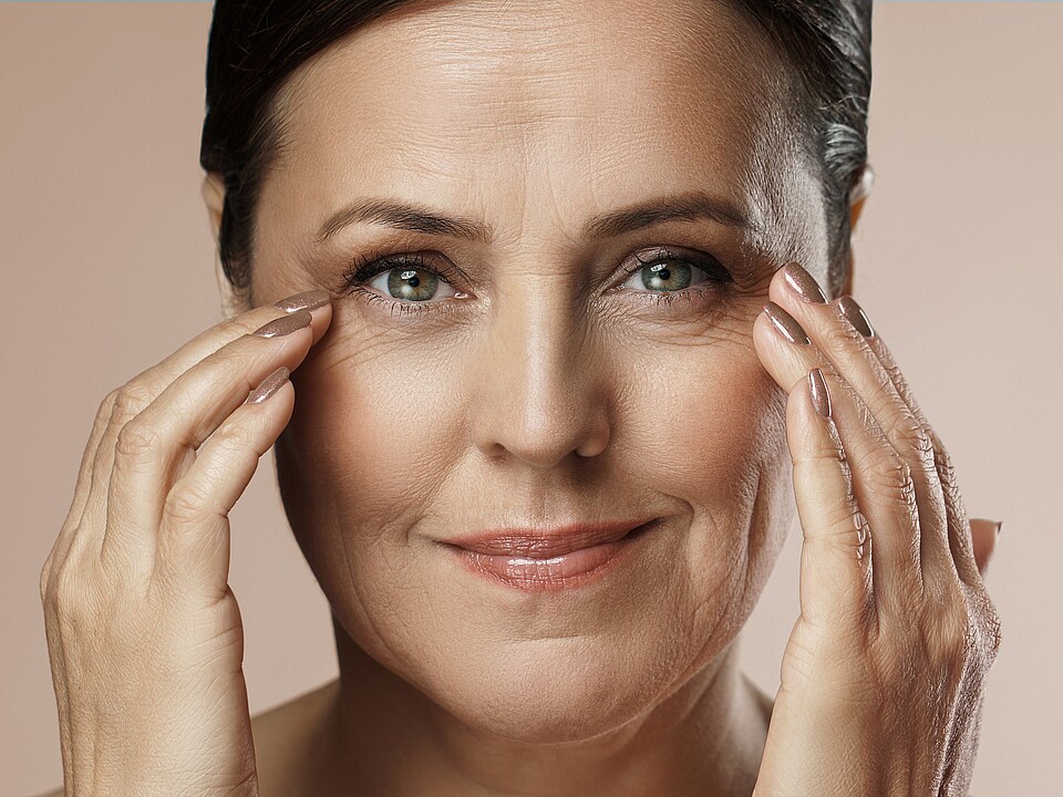 Lächelnde Frau berührt sanft ihre Haut – Symbol für ästhetische Behandlungen und Hautverjüngung.