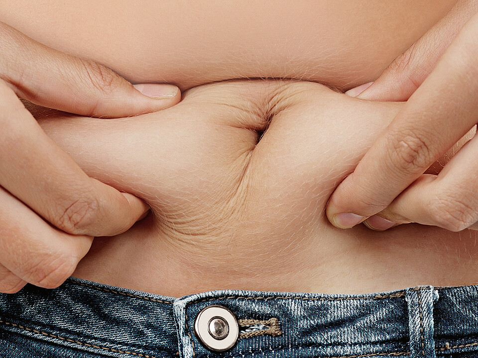 Nahaufnahme eines Bauchs, bei dem eine Person Hautfalten zwischen den Fingern hält